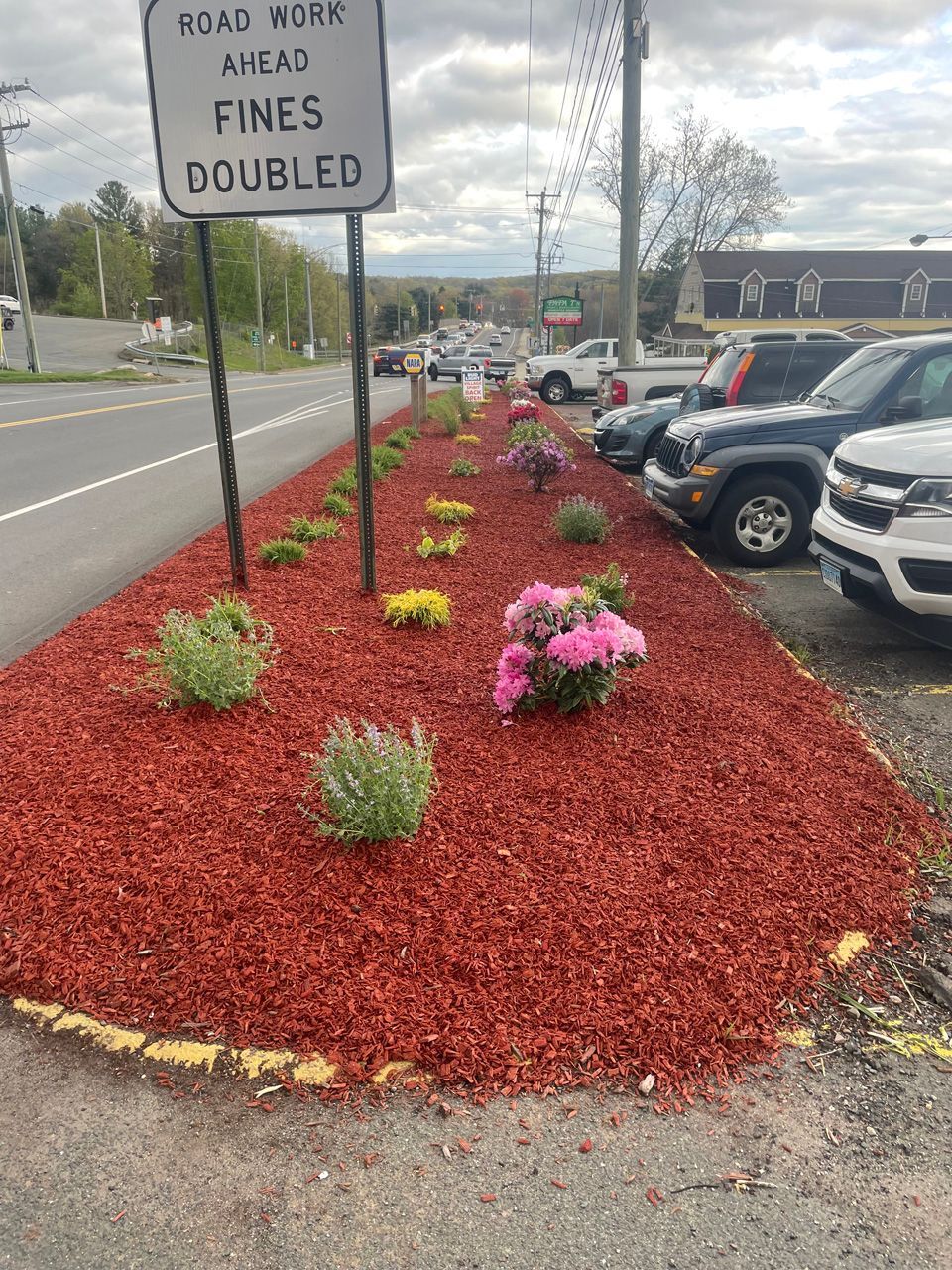 Parking lot landscaping with red mulch and pink flowers beside a sign reading “Fines doubled ahead.”