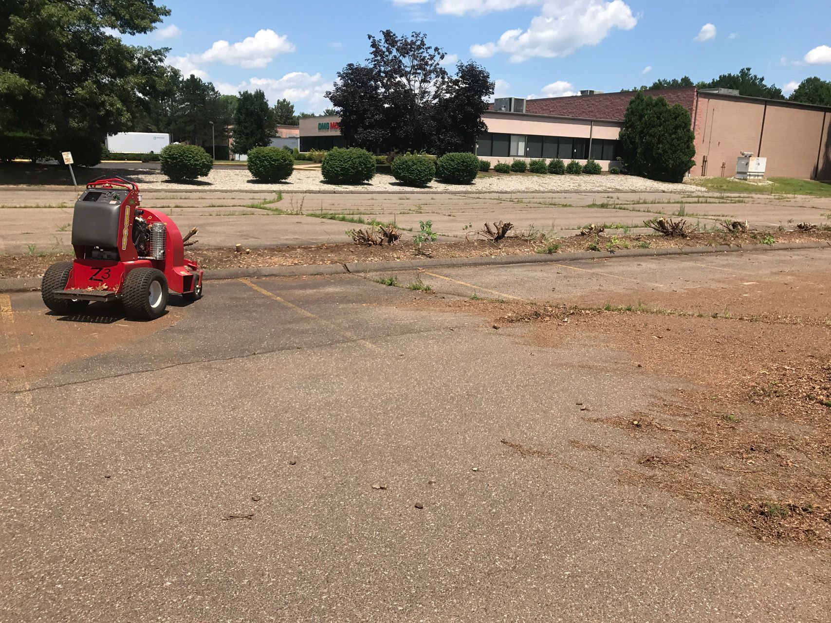 Red ride-on mower on gravel lot with buildings and trees in the background