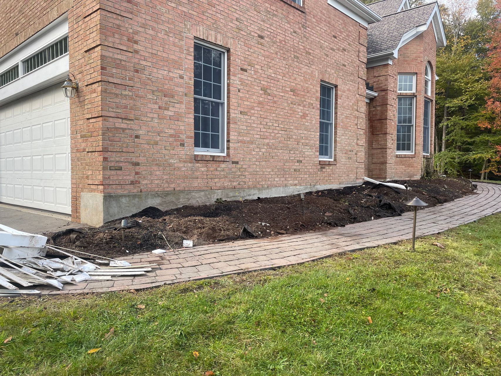Brick house with freshly dug foundation trench and disturbed soil along the side wall