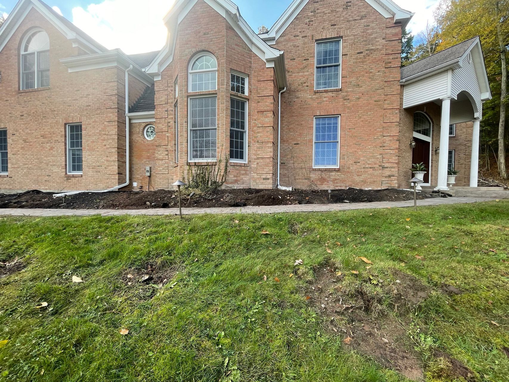 Brick house exterior with large windows, a covered porch, and a grassy front yard