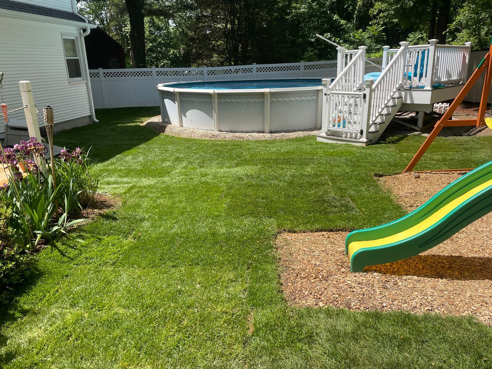 Backyard with above-ground pool, green lawn, flower bed, and a small slide