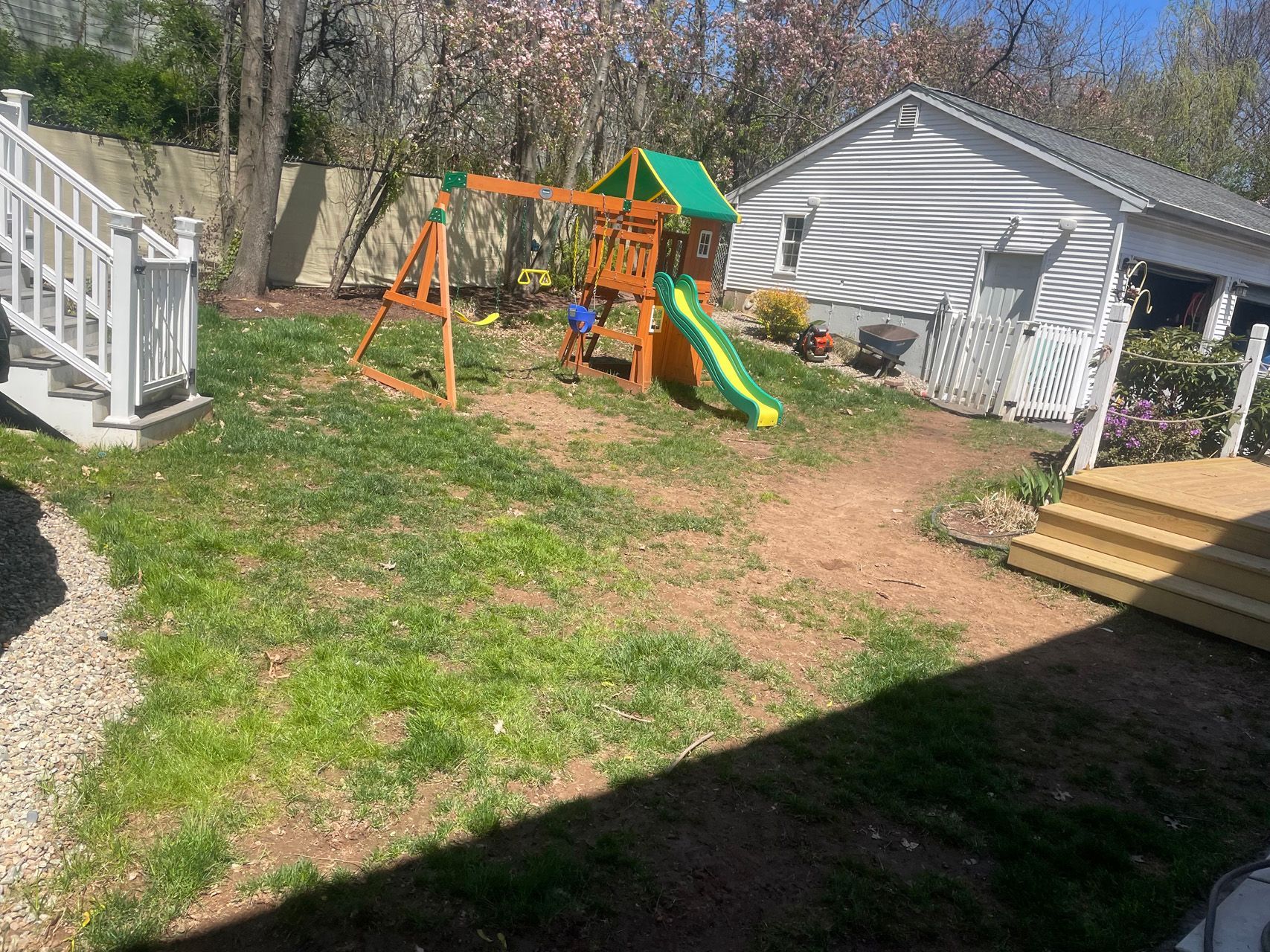 Backyard with a green-and-orange swing set and slide near a garage and wooden deck steps