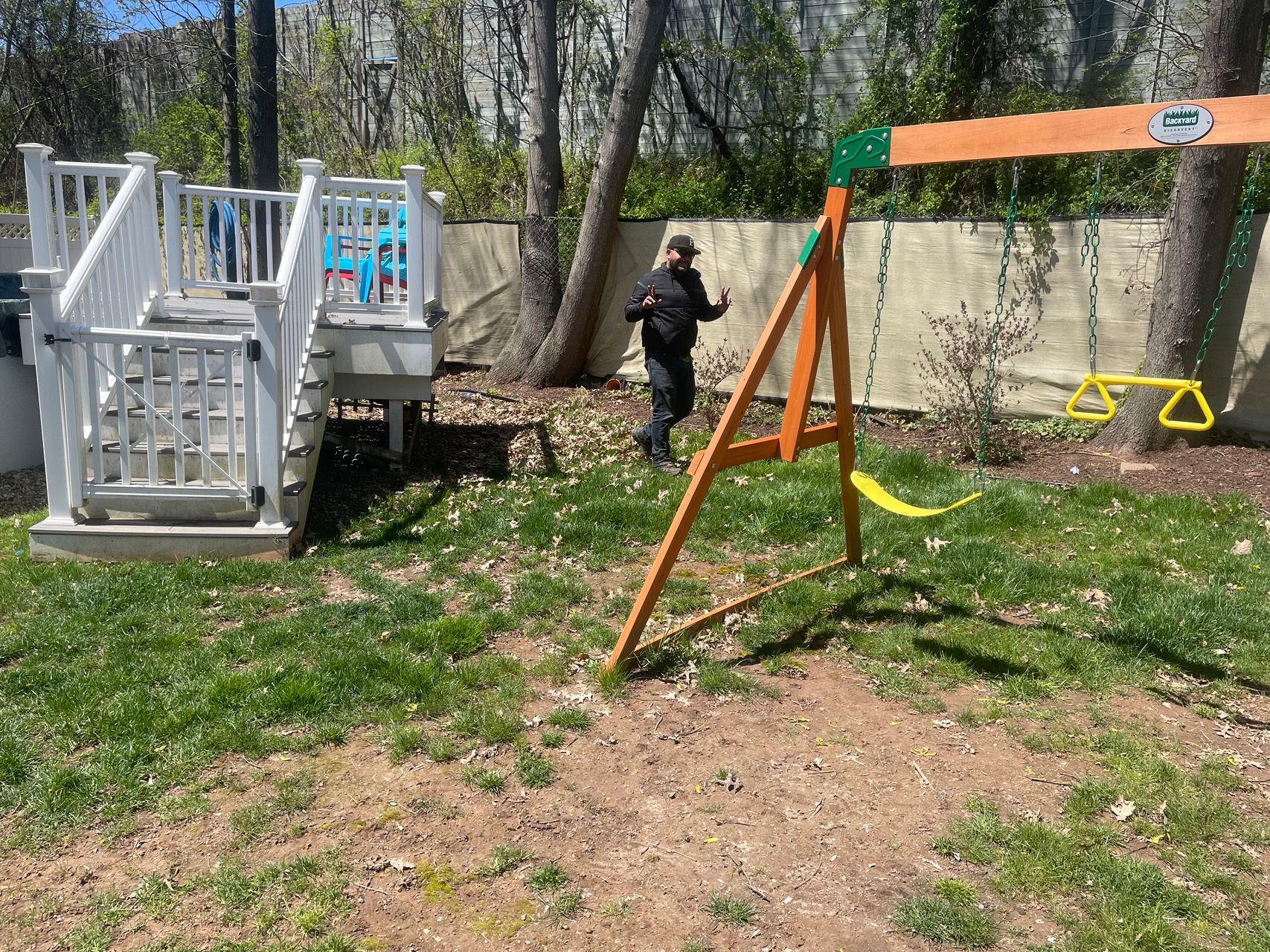 Backyard playground with playset, swing set, and a person near a wall