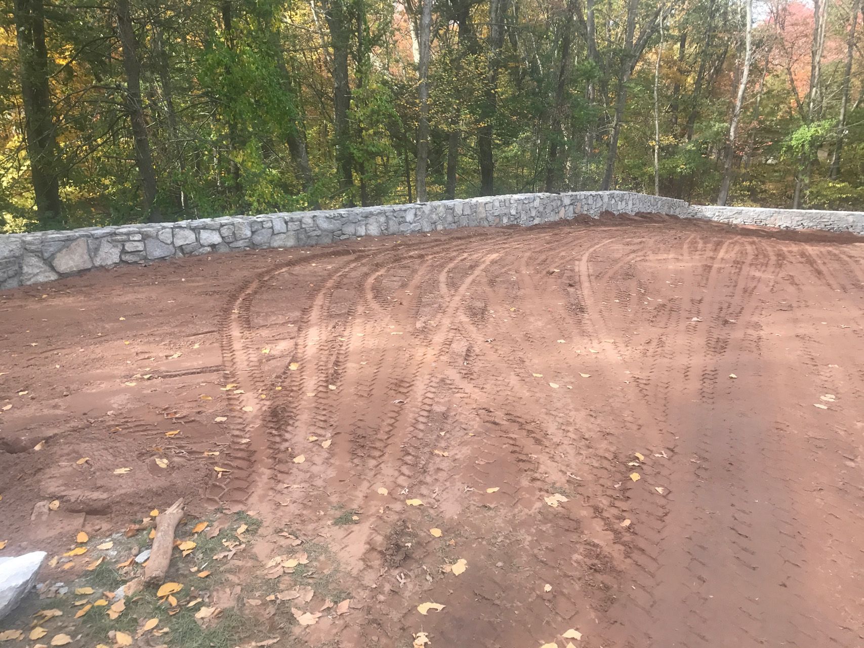 Freshly graded dirt lot beside a stone wall and trees in autumn