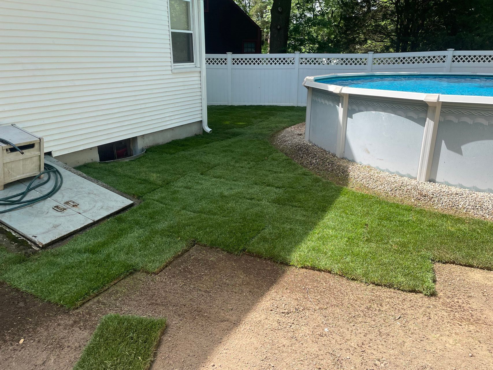 Backyard with above-ground pool, grass lawn, and side of a house with concrete patio.