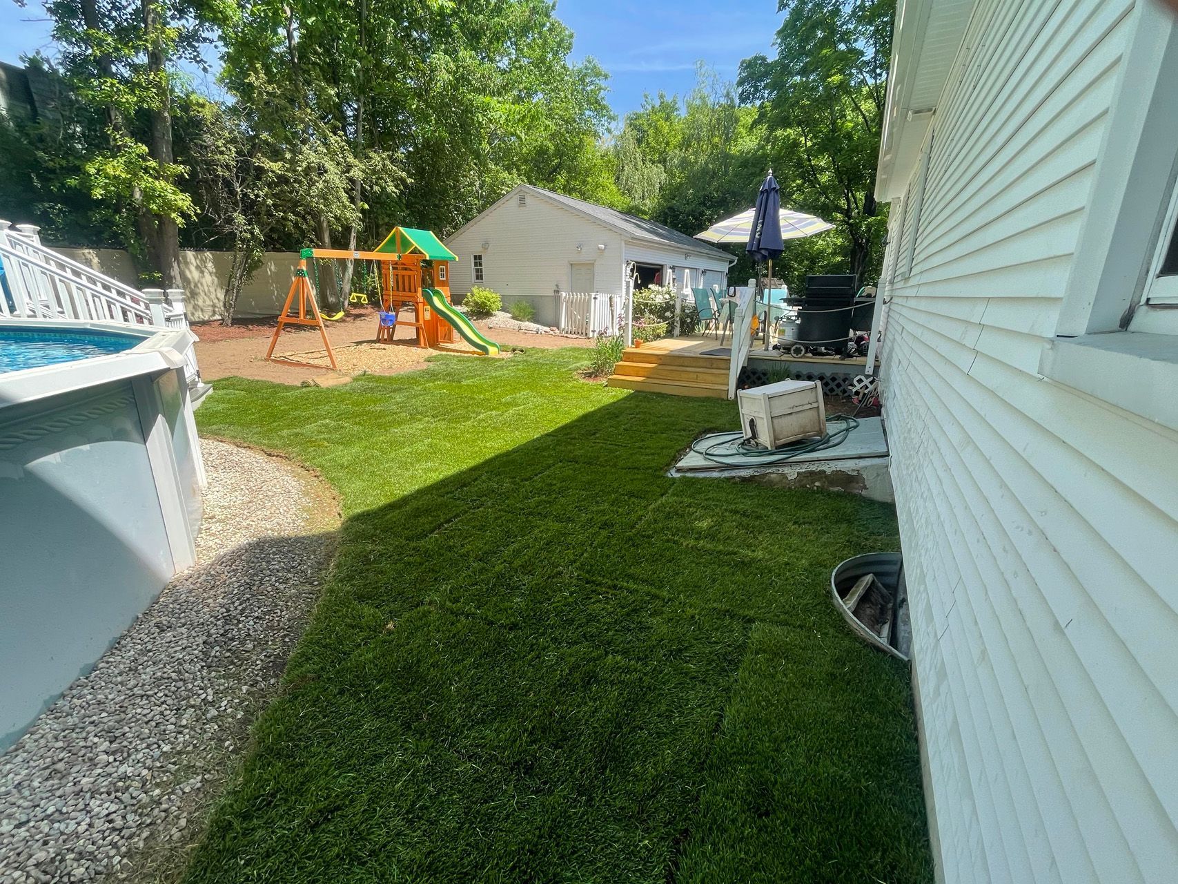 Backyard with playground, lawn, patio furniture, and house siding on a sunny day