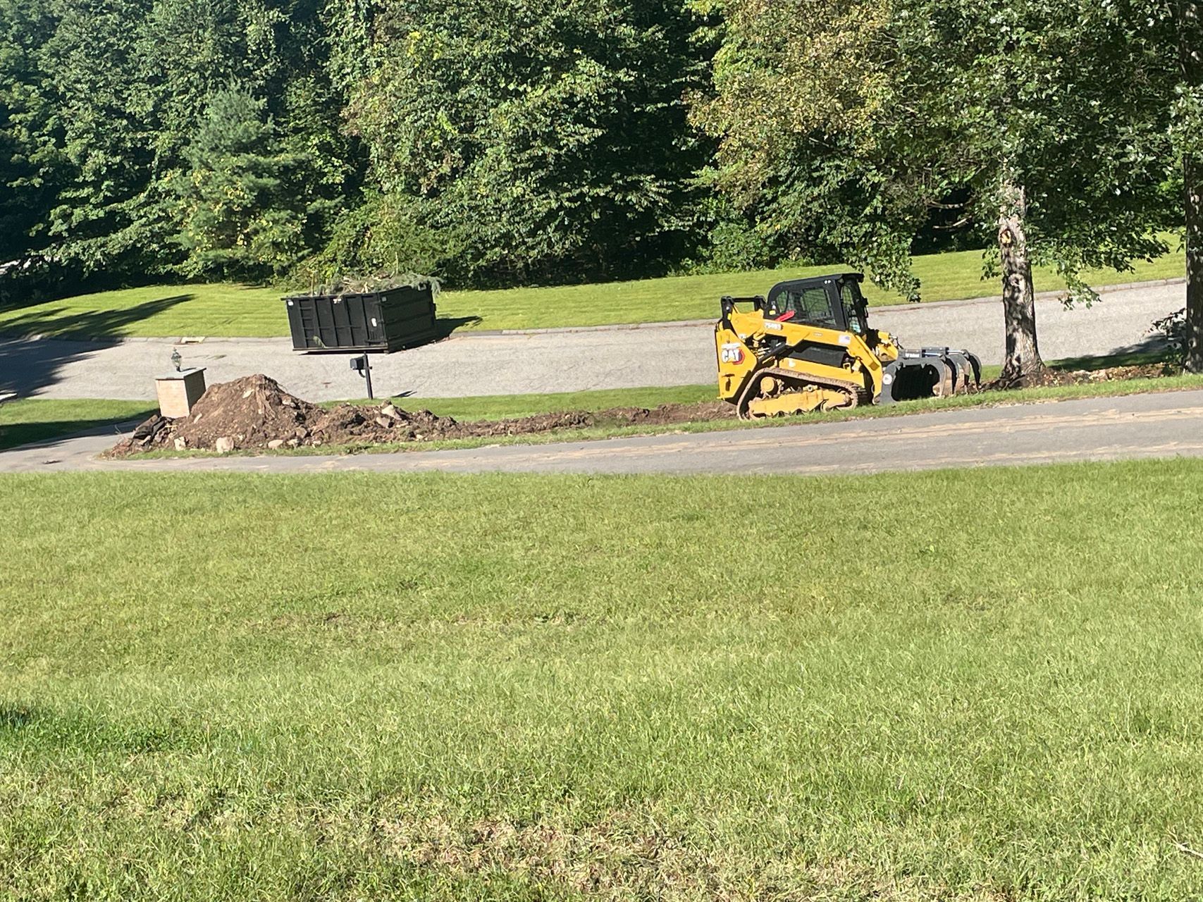 Yellow skid steer clearing dirt beside a road in a grassy park area