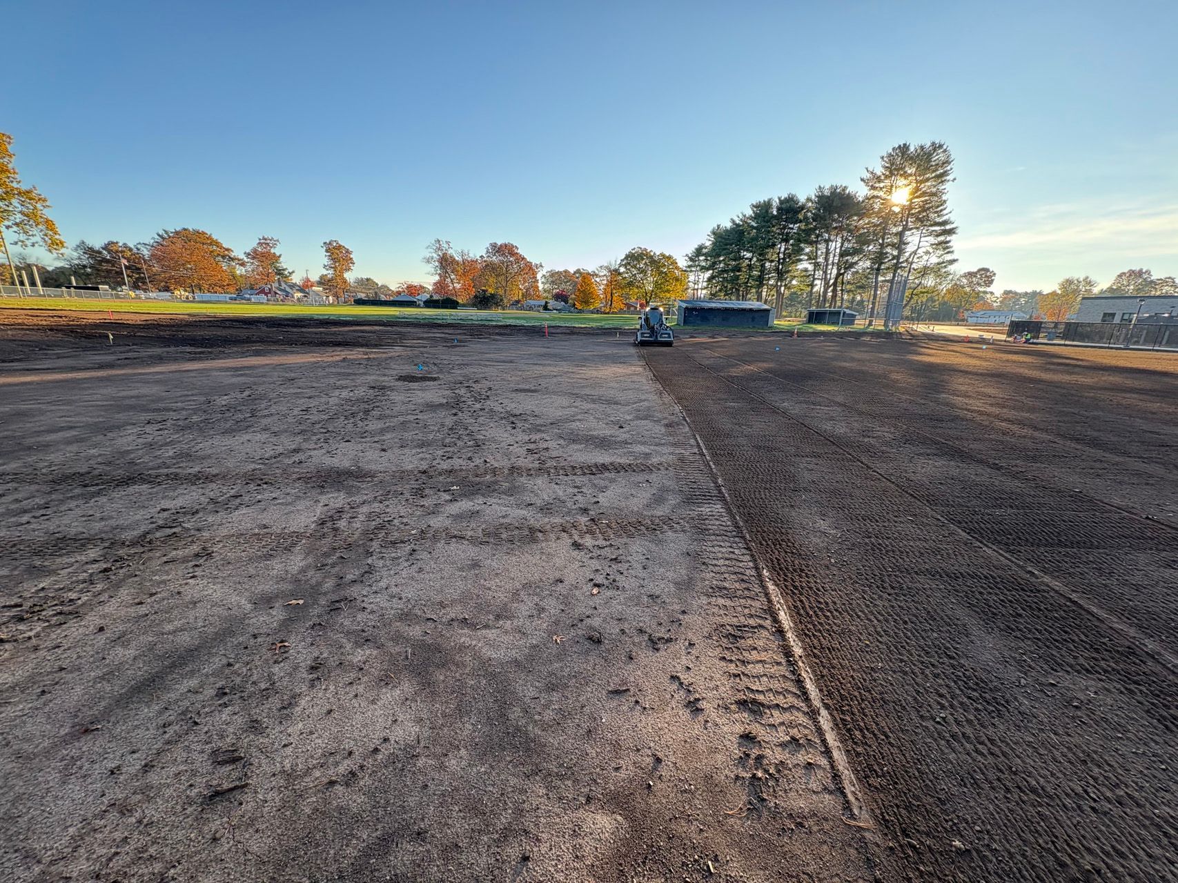 Wide gravel lot with a small vehicle in the distance under a clear sky at sunrise