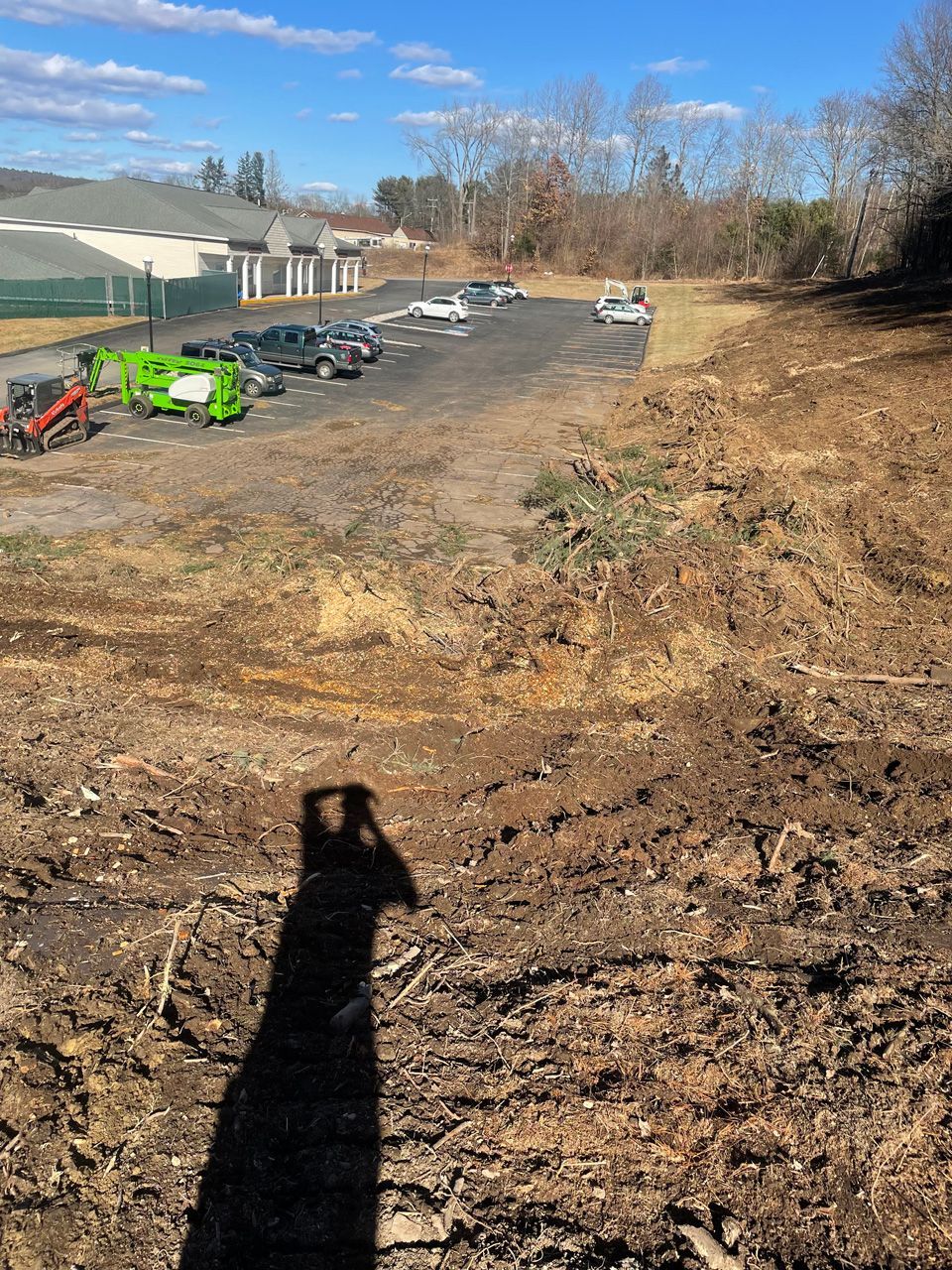 Gravel lot beside a greenhouse with parked equipment and a small white vehicle under a clear blue sky