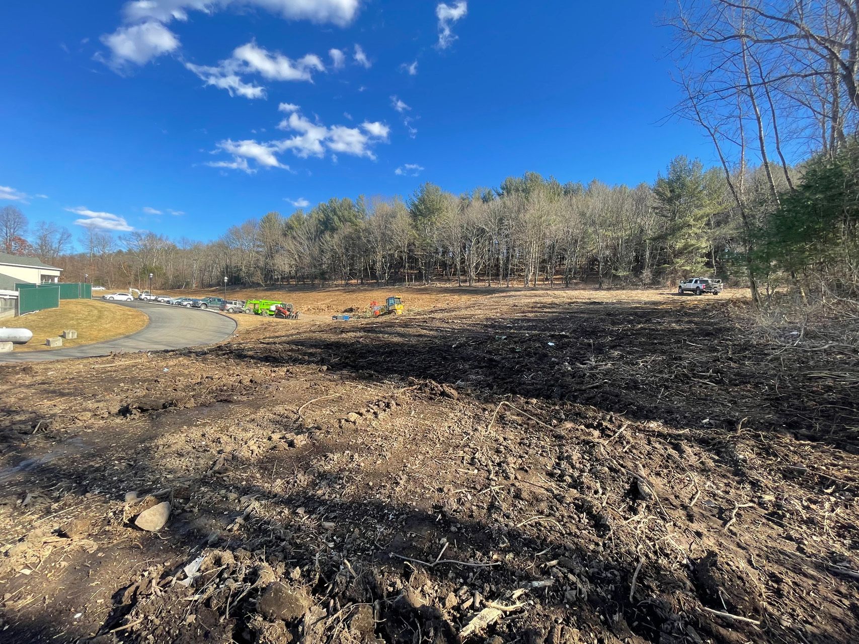 Wide muddy construction site under a bright blue sky with trees in the background
