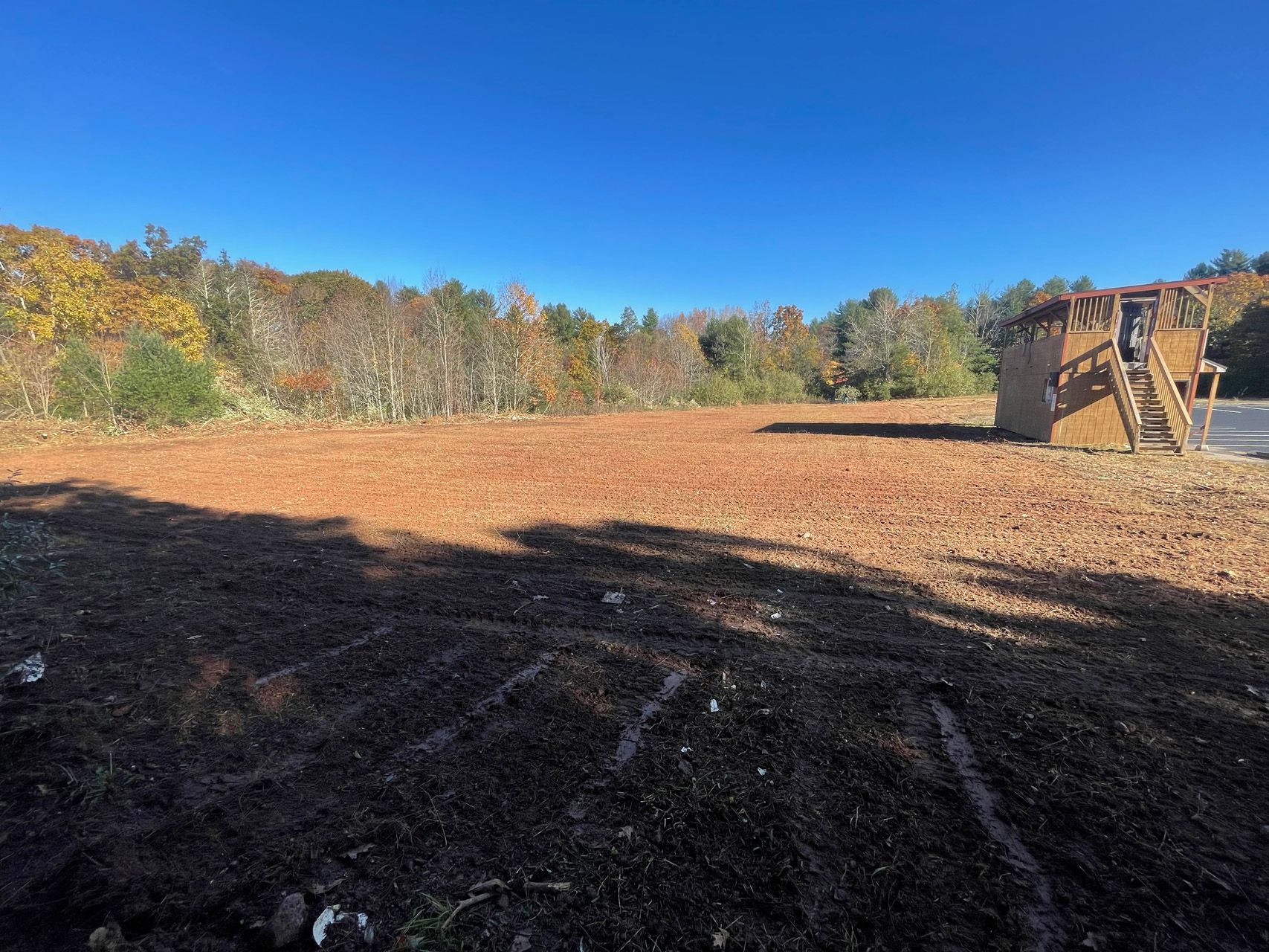Wide muddy field under blue sky with autumn trees and a bulldozer on the right