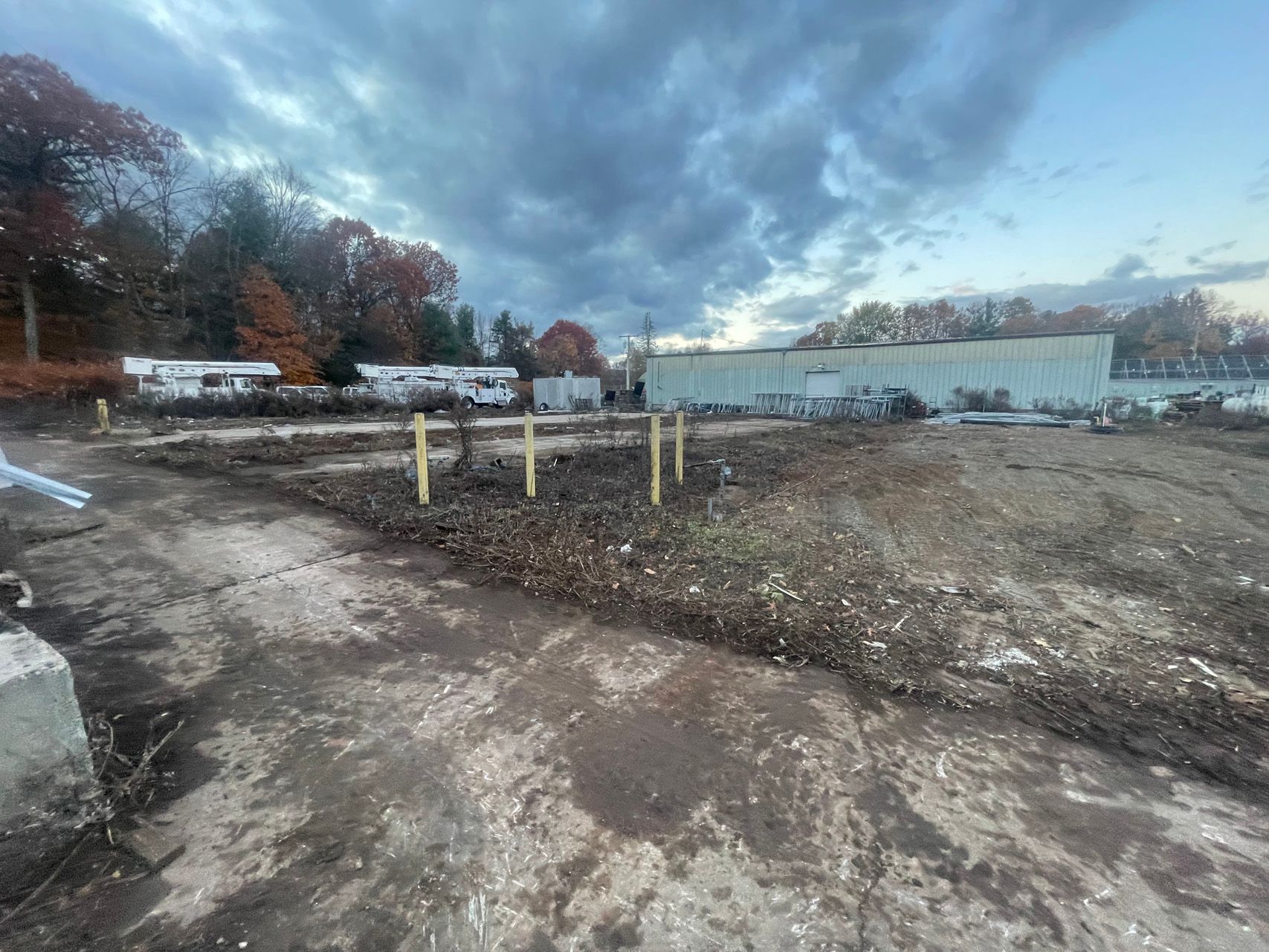 Bare lakeside construction site with dirt path, debris, and cloudy sky at dusk
