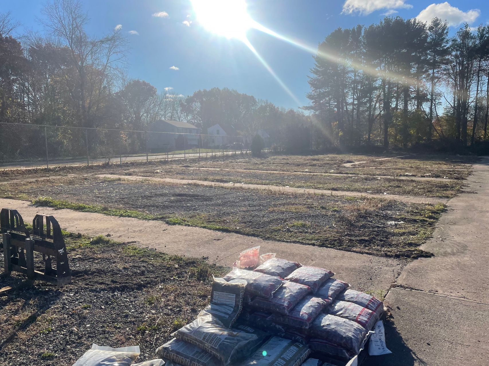 Sunny field with newly laid sod, a paved path, and stacked materials in the foreground