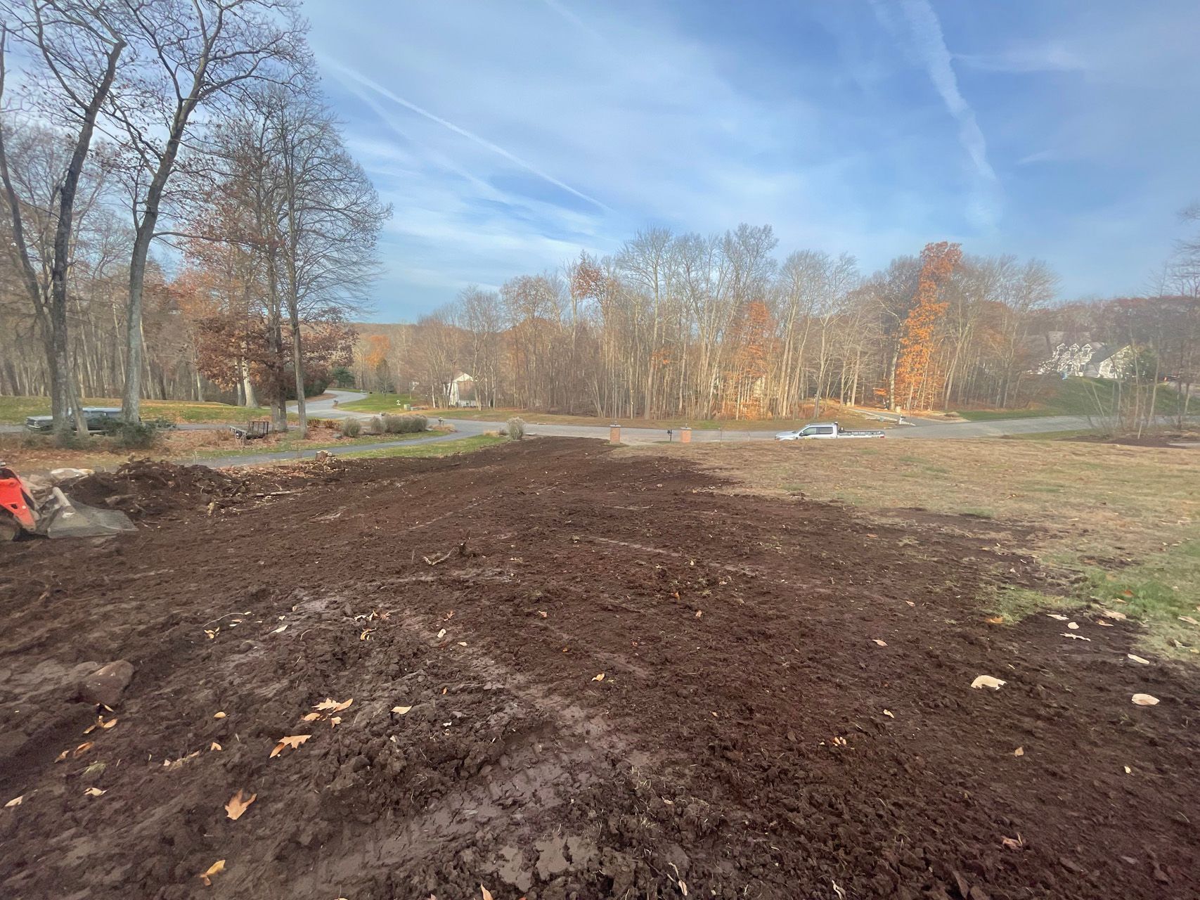 Freshly graded dirt lot beside leafless trees under a blue sky on a sunny day
