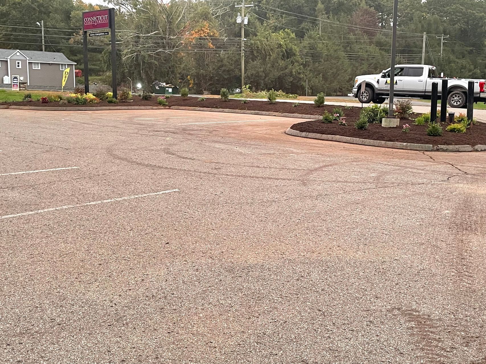 Wet parking lot with landscaped islands, trees, and a white pickup truck in the background