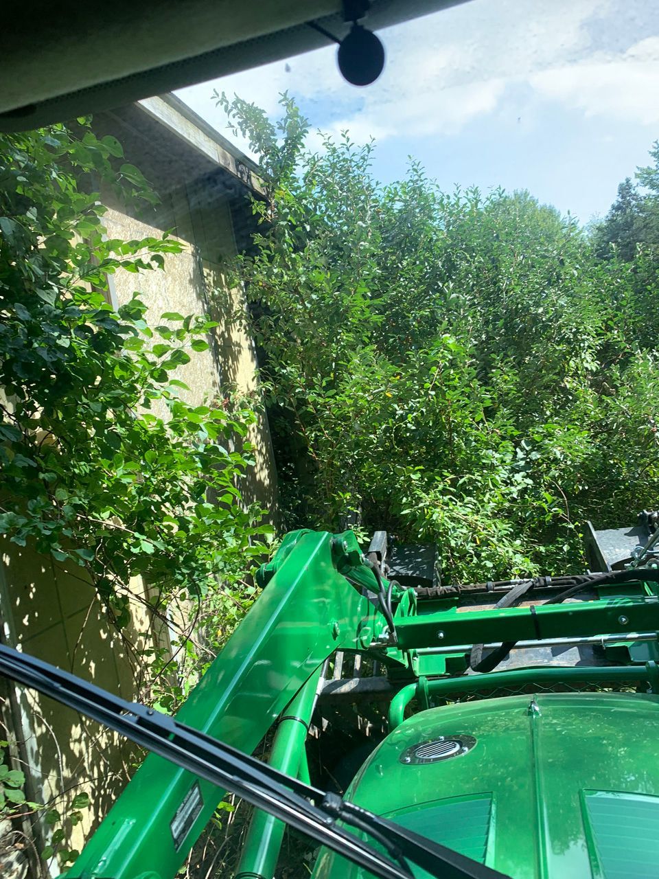 Green tractor working beside a house and trees in a sunny yard