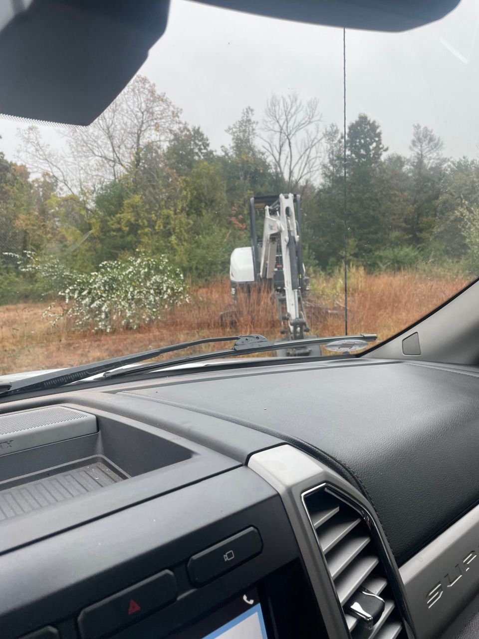 View from inside a vehicle toward a muddy trail and trees, with a white off-road machine ahead.