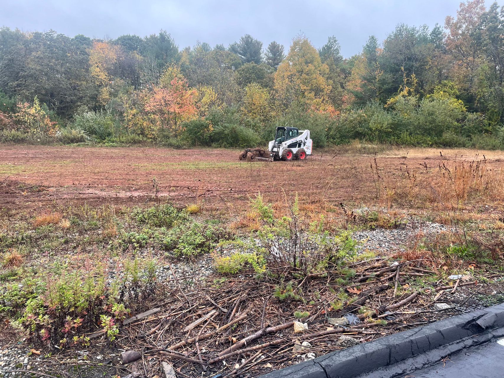 Small white utility vehicle in a plowed field with trees in fall colors behind it.