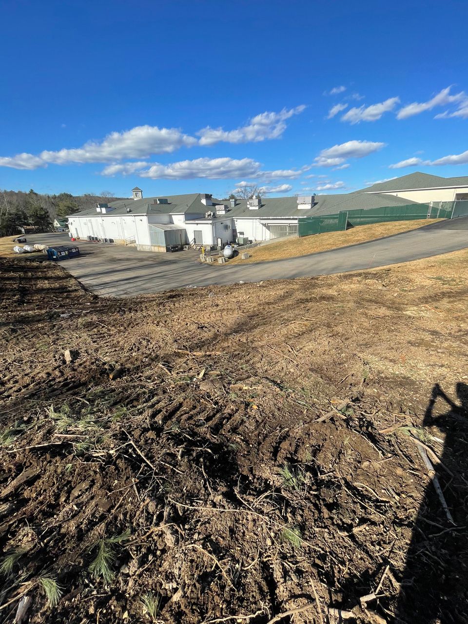 Rural farm buildings beside muddy ground under a bright blue sky, with hills in the background