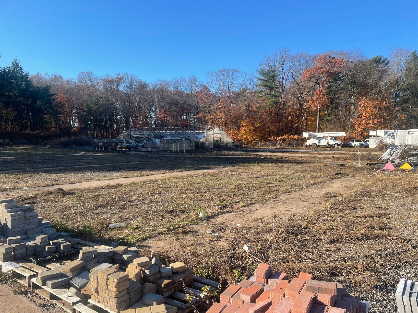 Cleared dirt lot with piles of bricks in the foreground and autumn trees lining the background