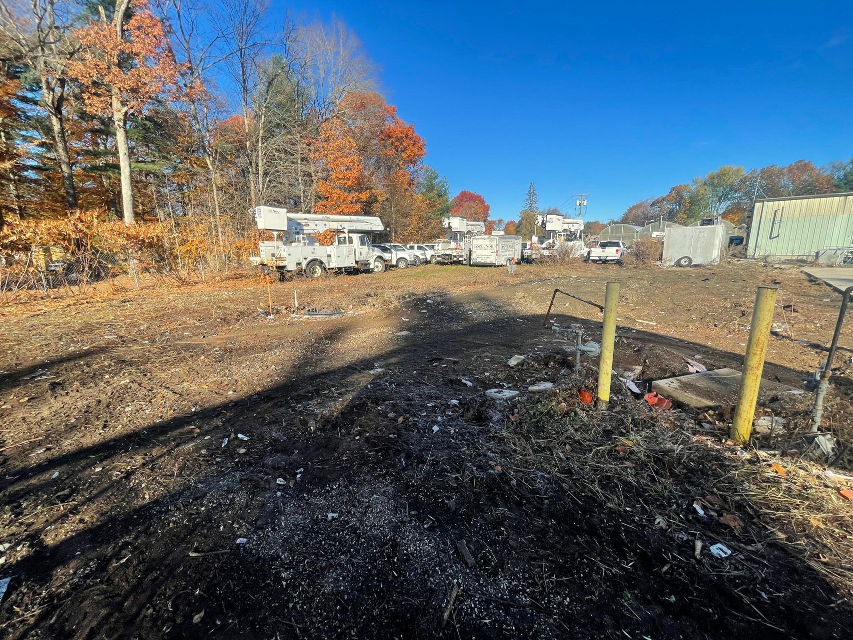 Autumn construction site with cleared dirt lot, trucks, and trees under a bright blue sky