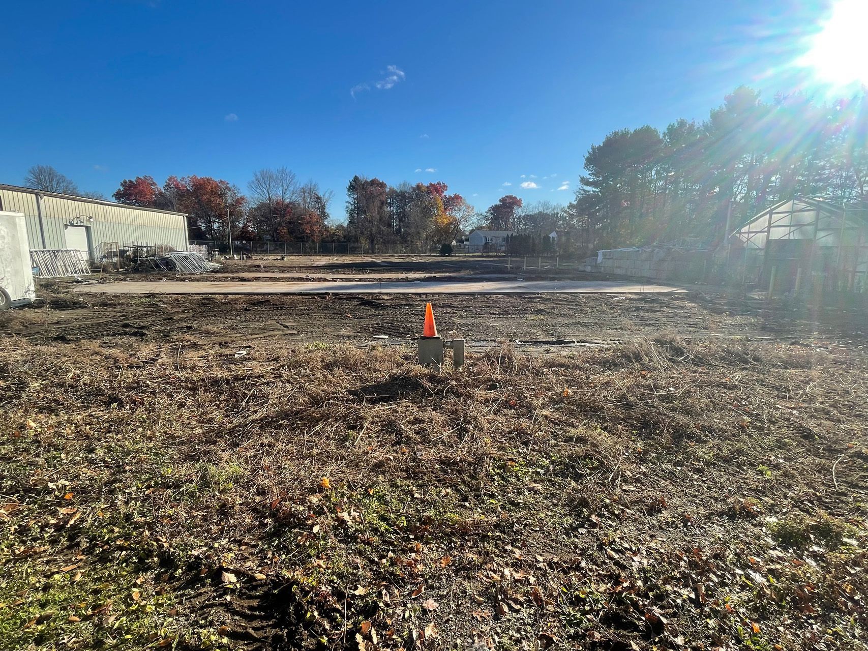 Empty grassy lot with an orange cone under bright sun and a clear blue sky