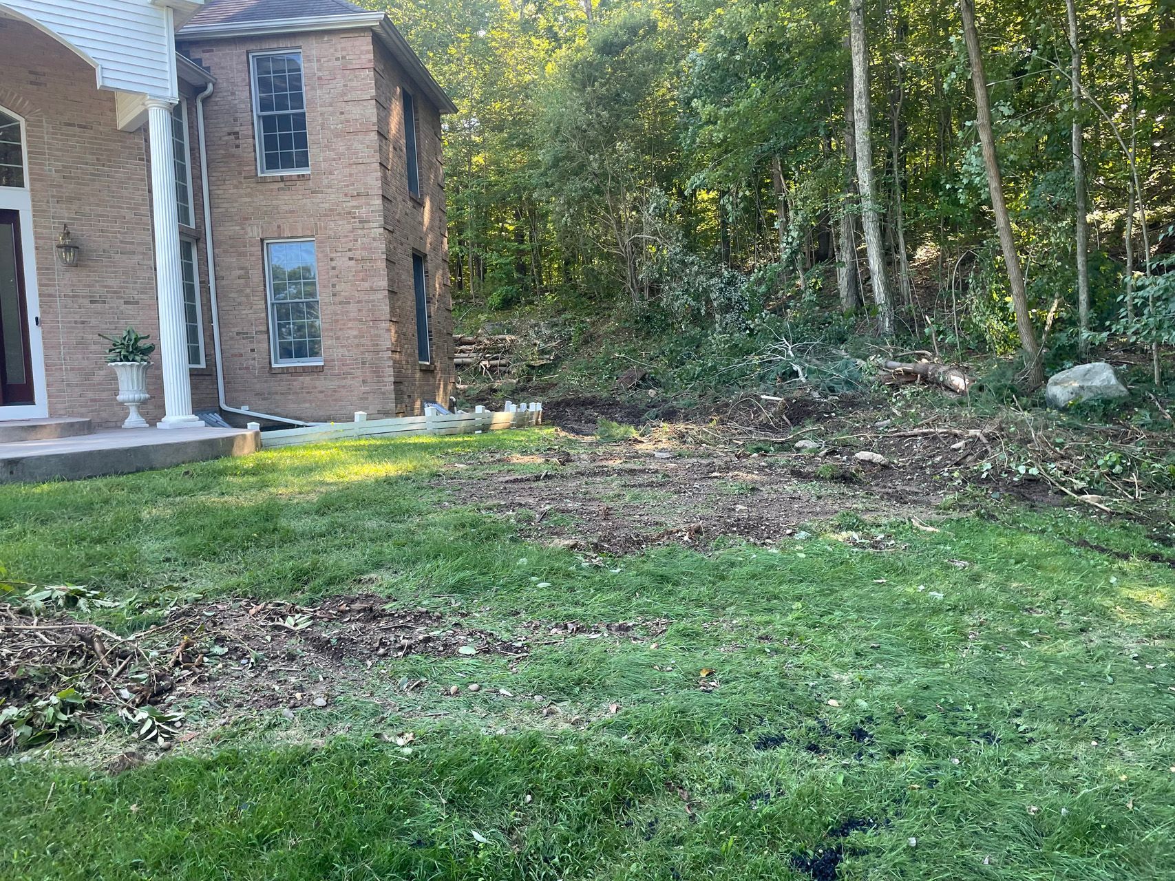 Backyard beside a brick house, with green grass, trees, and a cleared dirt patch