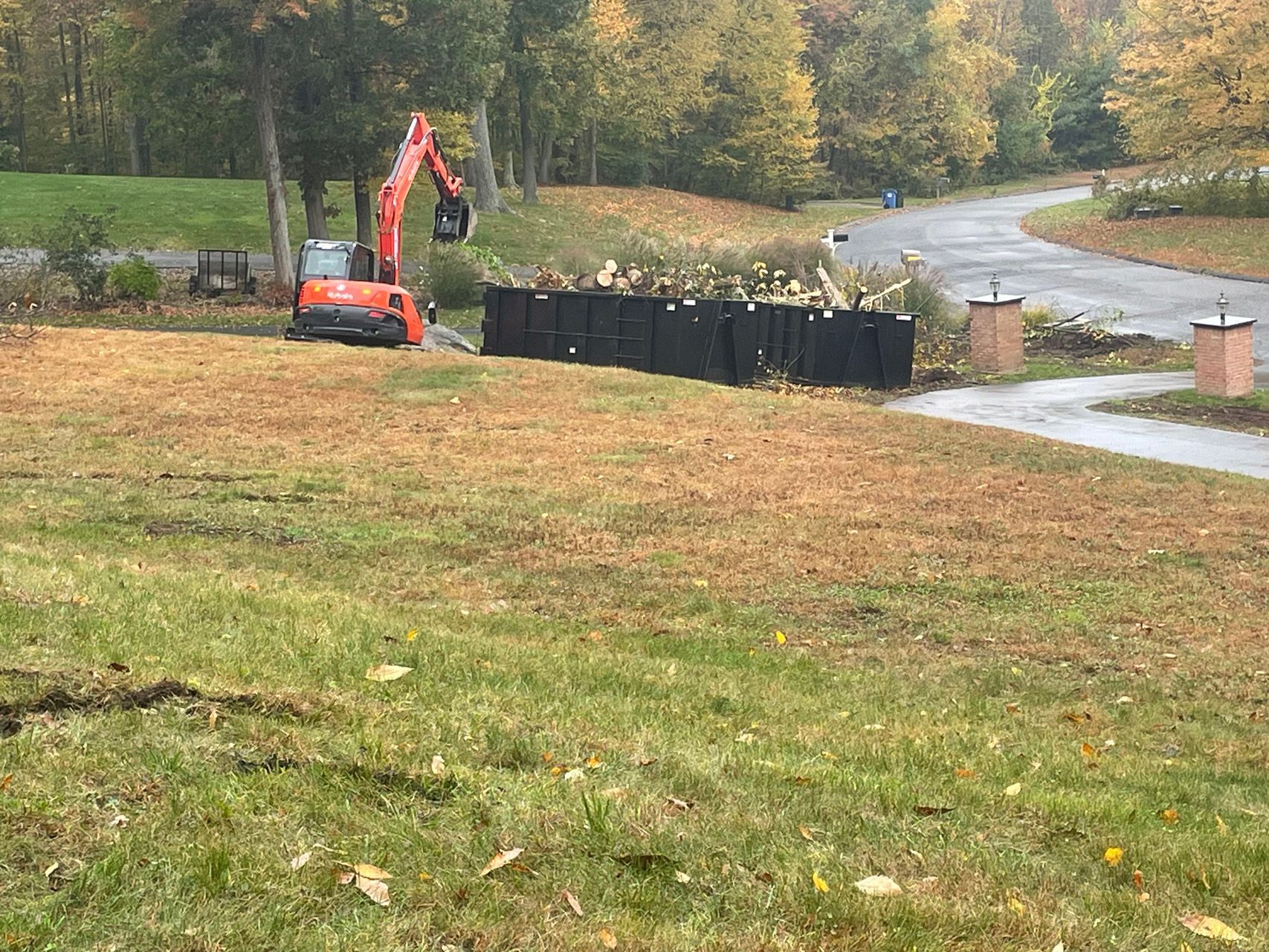Orange excavator beside black erosion-control barriers on a grassy roadside curve