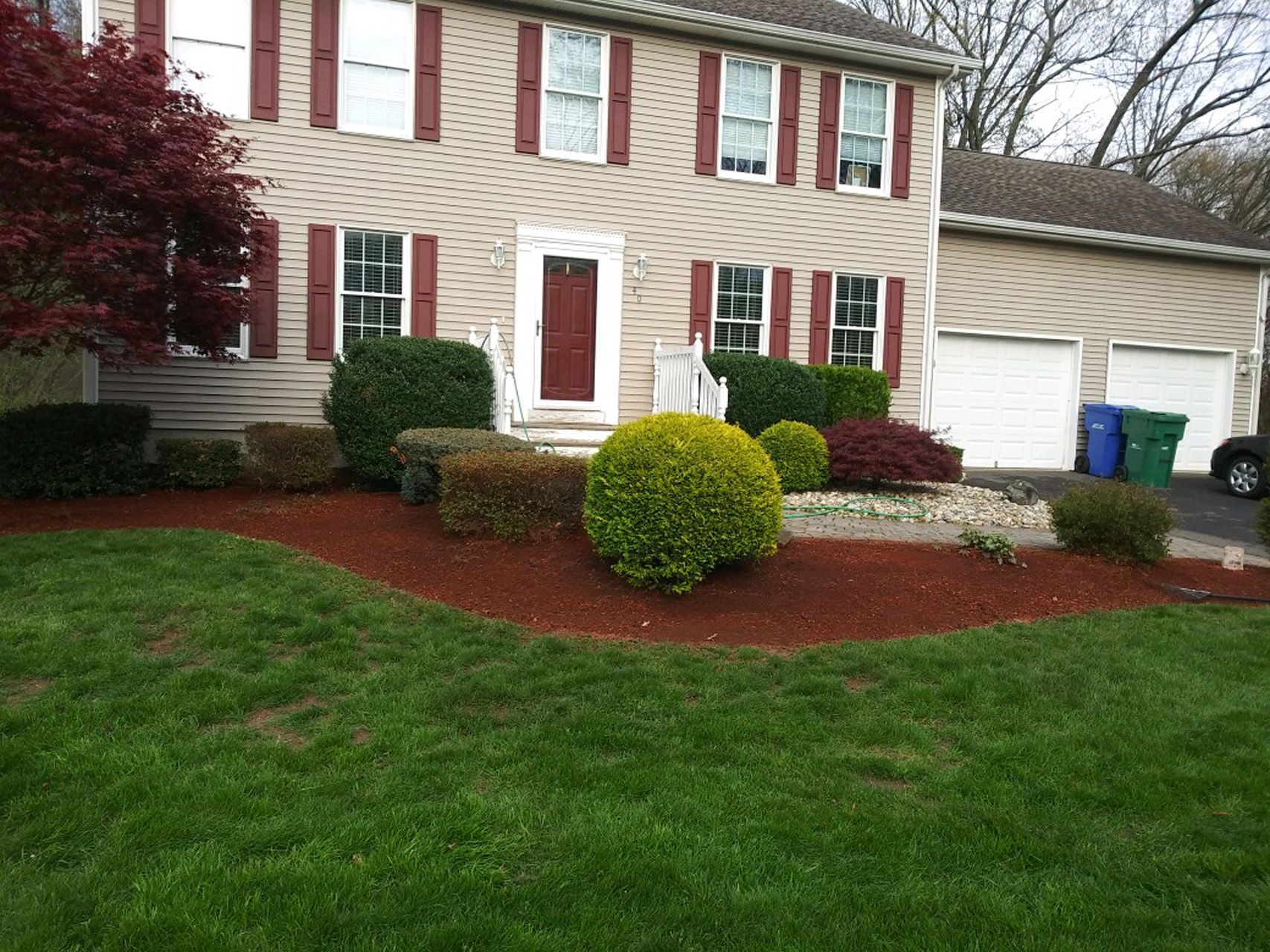 Suburban house with red shutters, white door, green lawn, and landscaped front yard