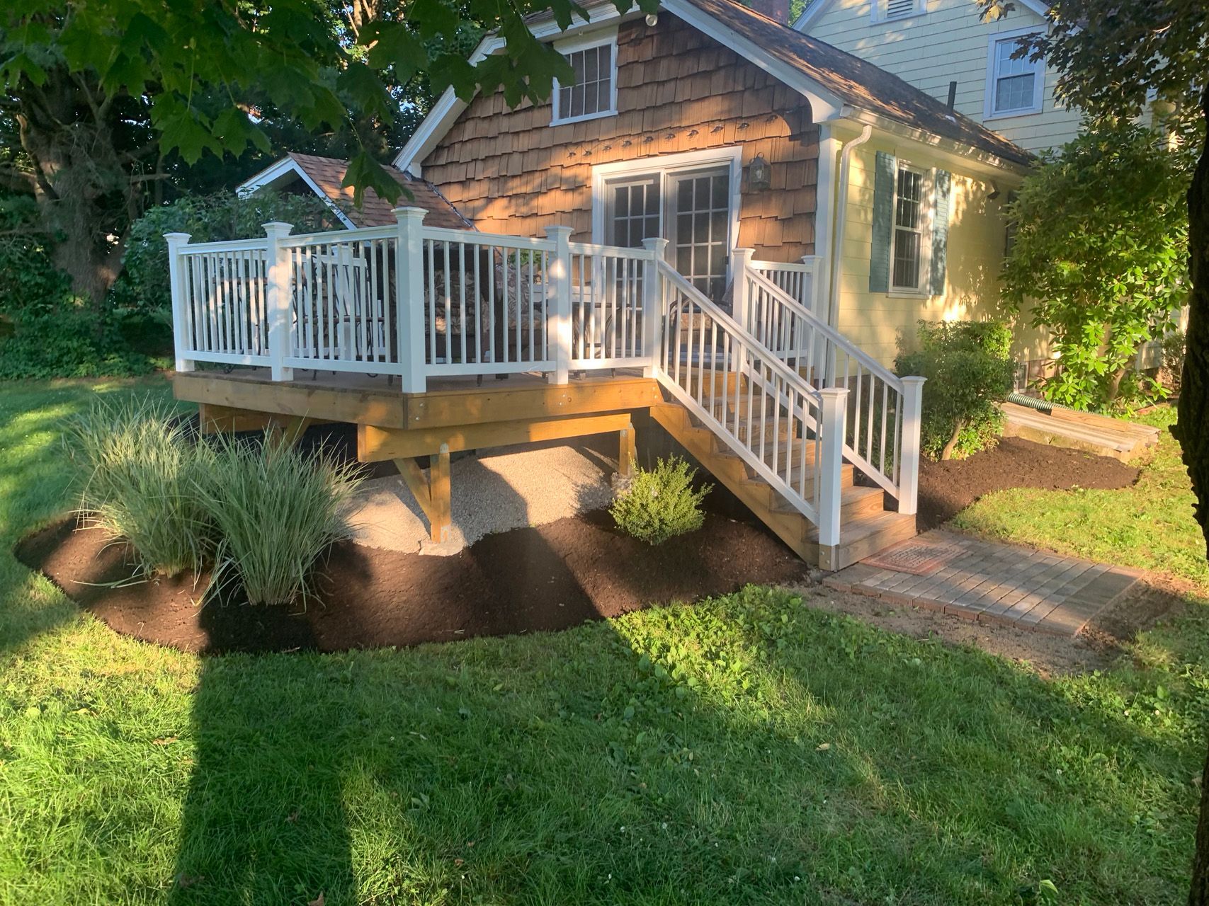 Small stone house with white porch railings, steps, and a lush green front yard at dusk