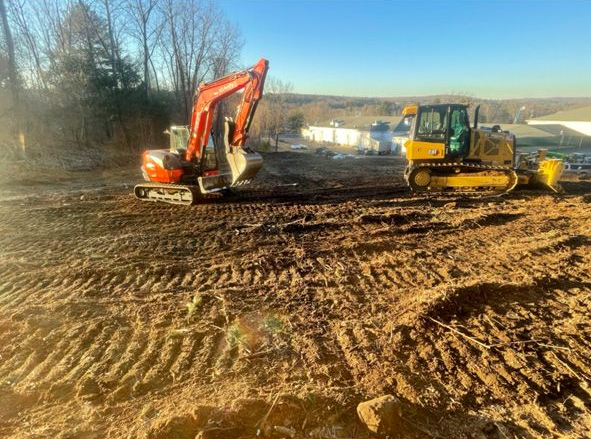Excavator and bulldozer working on a muddy construction site under a clear blue sky
