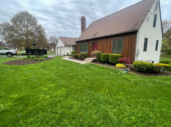 Rural farmhouse with red barn, white house, and green lawn under a cloudy sky