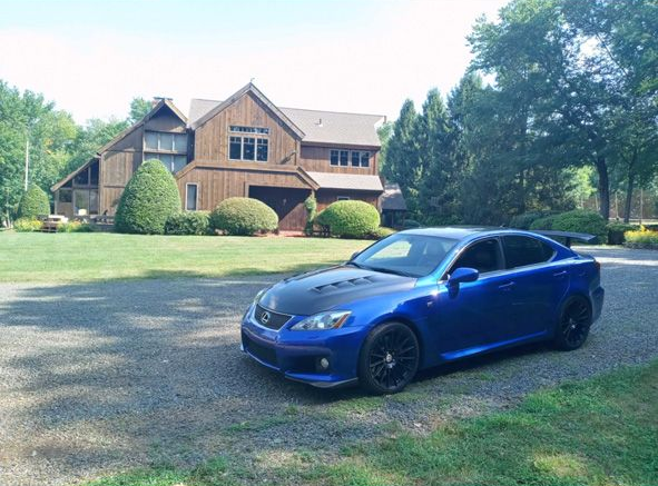 Blue car parked on a grassy driveway in front of a large house with trees around it