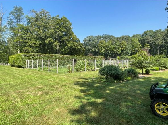 Sunny field with white fence, trees, and a green tractor in the foreground