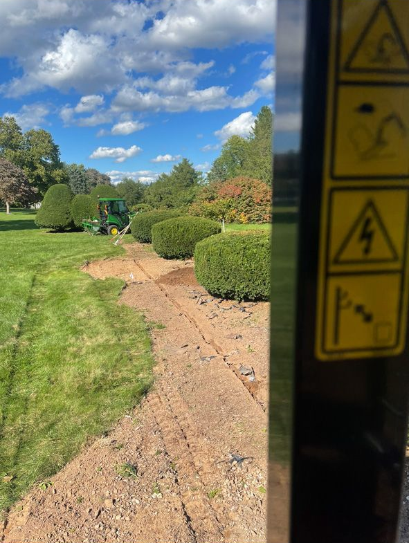 Gravel path through a green garden under a blue sky, viewed past a doorway with caution stickers.
