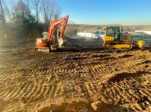 Orange excavator and yellow bulldozer working on a muddy construction site under a blue sky