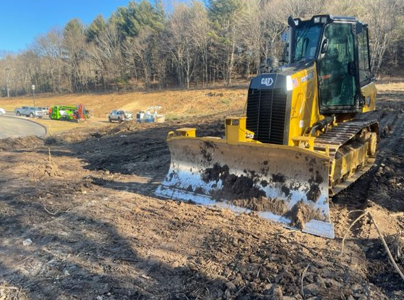 Yellow bulldozer on a muddy construction site near a tree line
