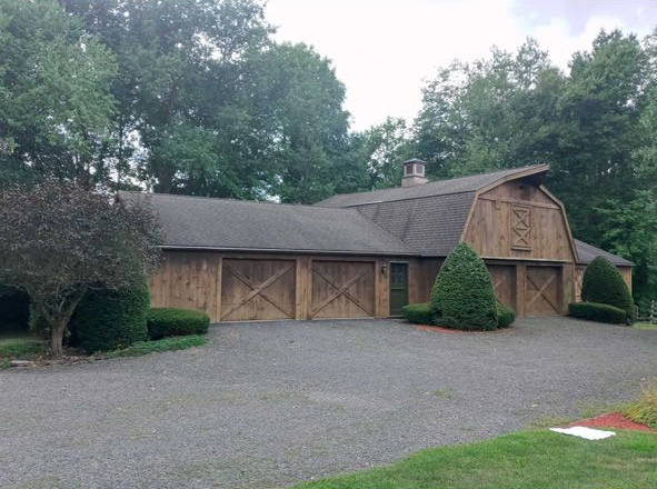 Large rustic wooden building with a gravel driveway, surrounded by trees under an overcast sky.