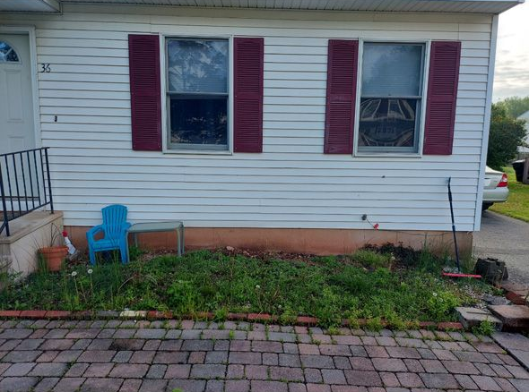 Small white house exterior with red shutters, a blue bucket, and a brick walkway in front.