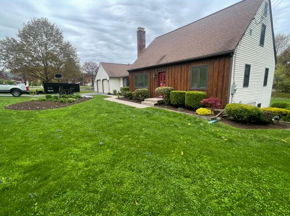 House with white siding and red barn-style extension beside a green lawn under a cloudy sky
