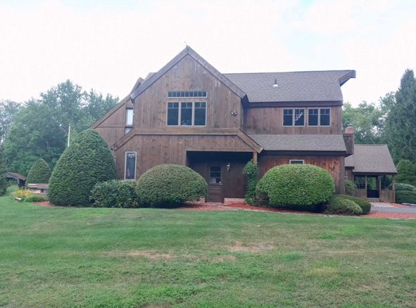 Brick house with a front lawn, shrubs, and a large gabled roof under an overcast sky