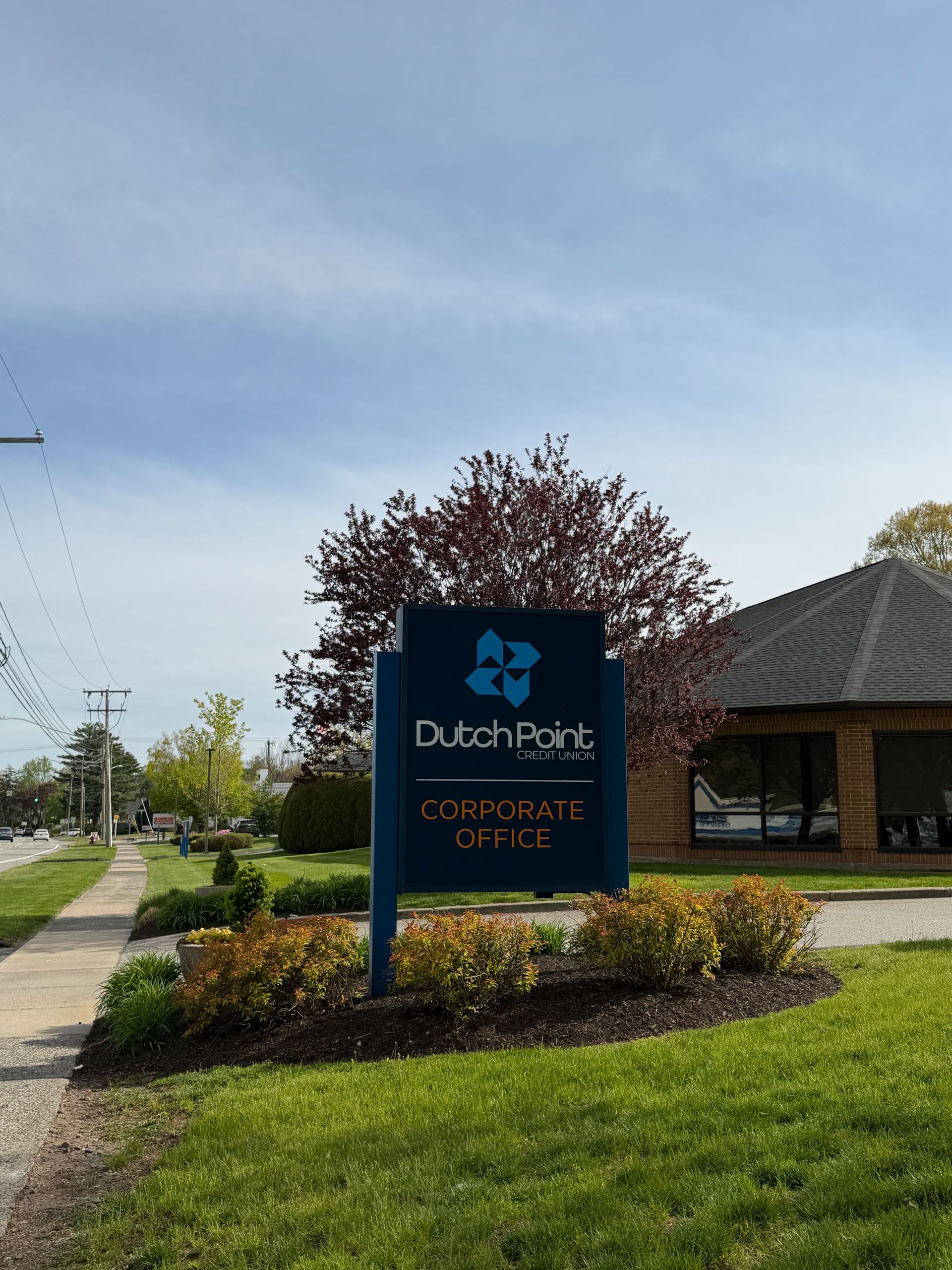 Dutch Bros Coffee sign beside a sidewalk in a landscaped parking lot on a sunny day
