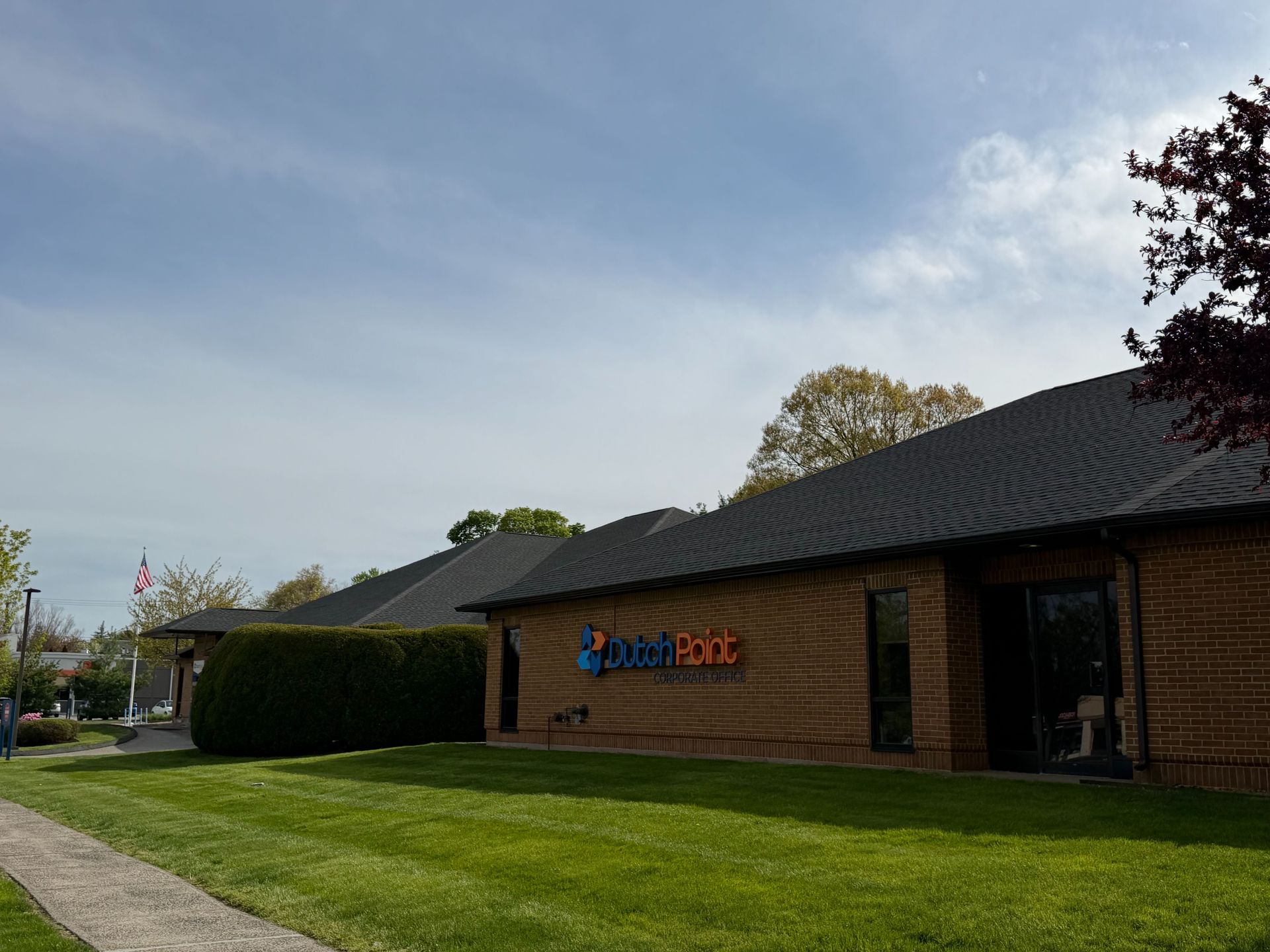Brick office building with blue and orange sign, sloped dark roof, and a green lawn under a clear sky