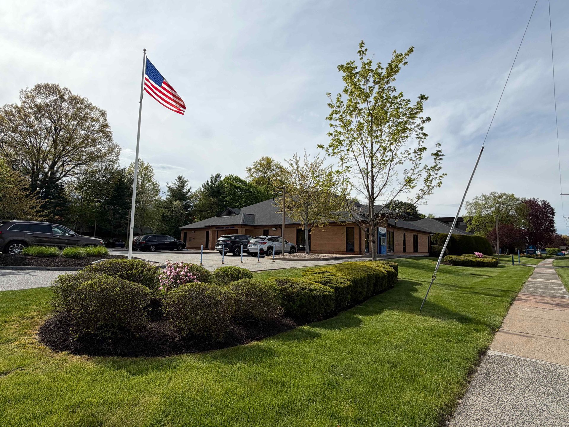 American flag flying by a small brick building with a grassy lawn and sidewalk on a sunny day