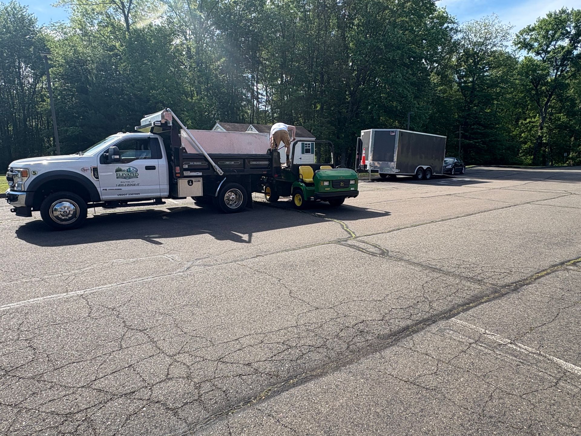 Work truck and trailer parked in a lot, with trees in the background.