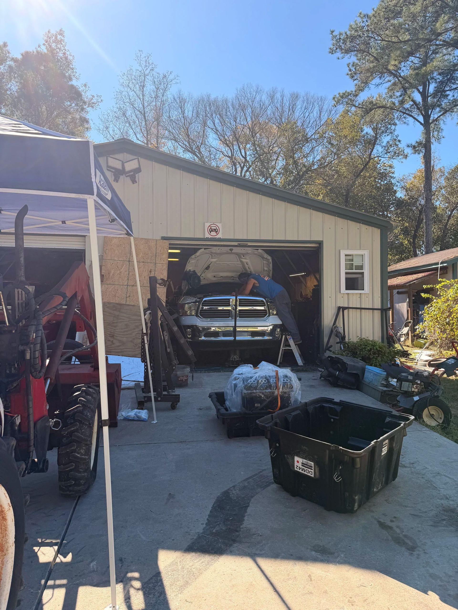 Detached garage with open door, two vehicles inside, and tools and bins scattered in the driveway.