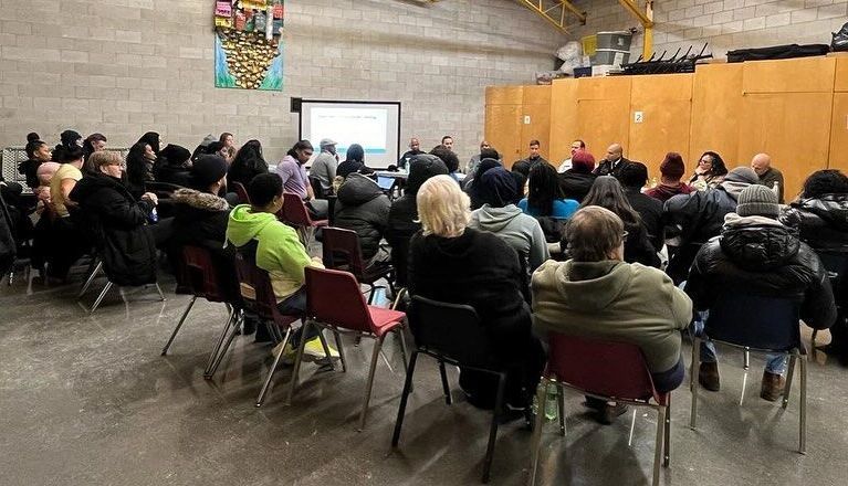 a large group of people are sitting in chairs in front of a projector screen