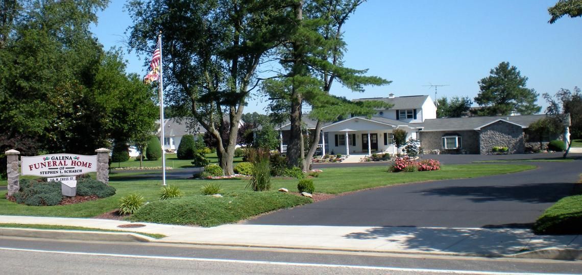 Suburban apartment entrance with a sign, flagpole, trees, and parked cars on a sunny day