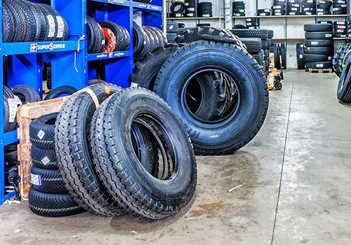Pneumatici impilati in un'officina meccanica con scaffalature blu e pavimento in cemento.