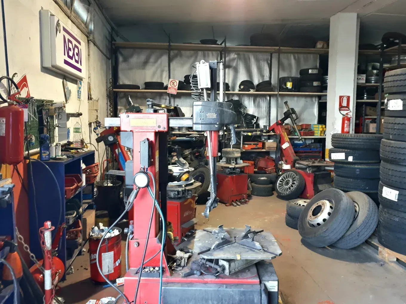 Officina meccanica disordinata con pneumatici, attrezzi e attrezzature riposti sotto scaffalature industriali.